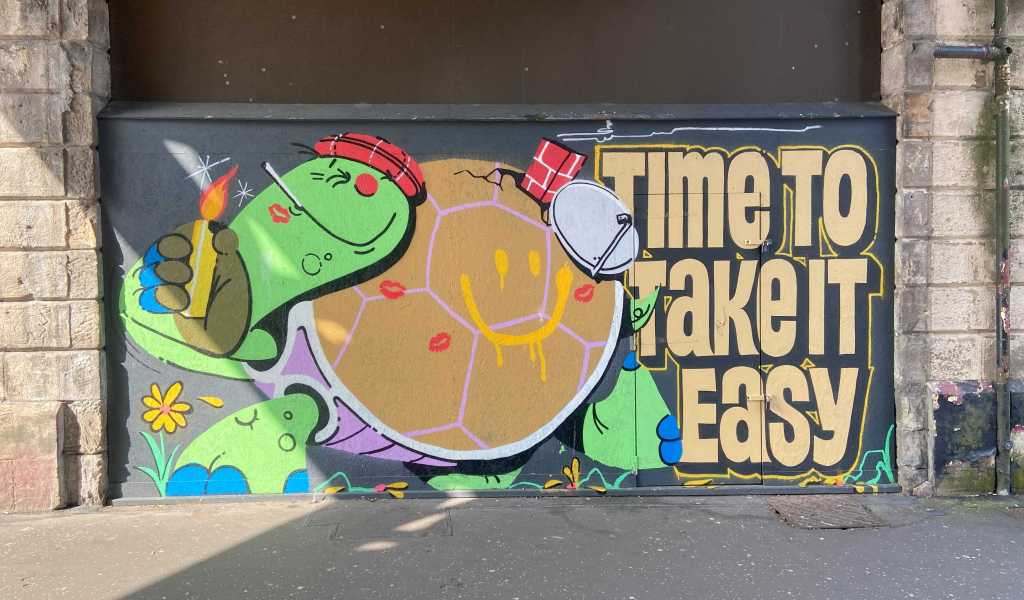 Glasgow street mural showing a tortoise lighting a cigarette and wearing a tartan bonnet and a caption 'Time to take it easy'. Artist unknown. Image credit: Ian Lacey.